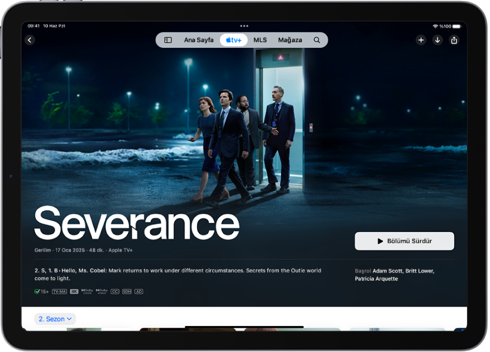 Öne çıkan bir Apple Original’ı adıyla, Oynat düğmesiyle ve bir bölüm açıklamasıyla birlikte gösteren Apple TV+ sekmesi. Ekranın en üstünde, soldan sağa doğru Ana Sayfa, Apple TV+, MLS, Mağaza ve Ara sekmeleri var.